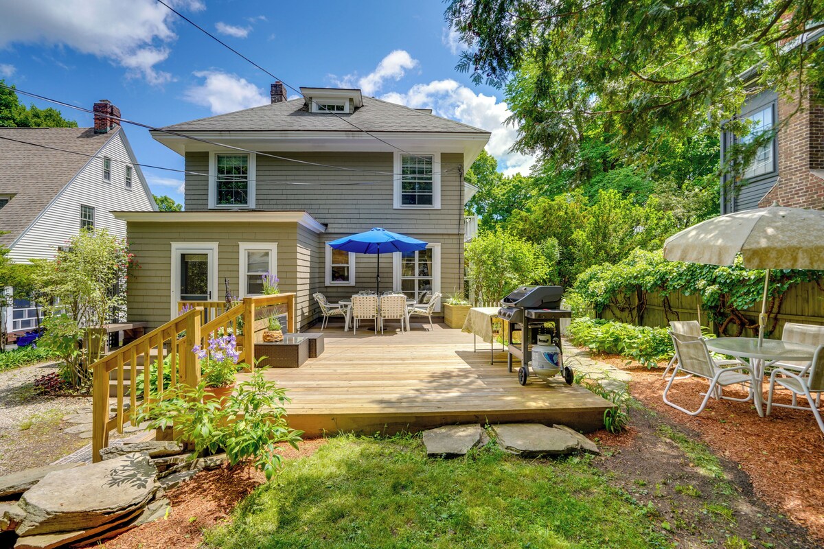A two-story house with a wooden deck, outdoor seating, and a barbecue area.