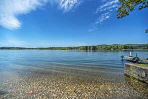 Un lago tranquilo con aguas transparentes, un muelle y una orilla distante con árboles y colinas.