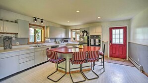 A kitchen with a central island, bar stools, and a red door. - Lakeside Berkshires Home Near Hiking & Skiing! (Lanesborough)