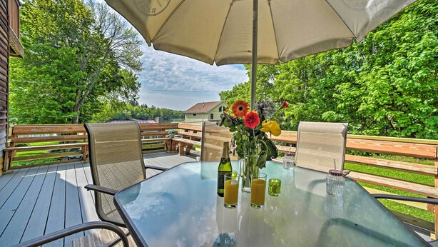 An outdoor patio with a glass table, two chairs, a beige umbrella, and a vase of flowers. - Lakeside Berkshires Home Near Hiking & Skiing! (Lanesborough)