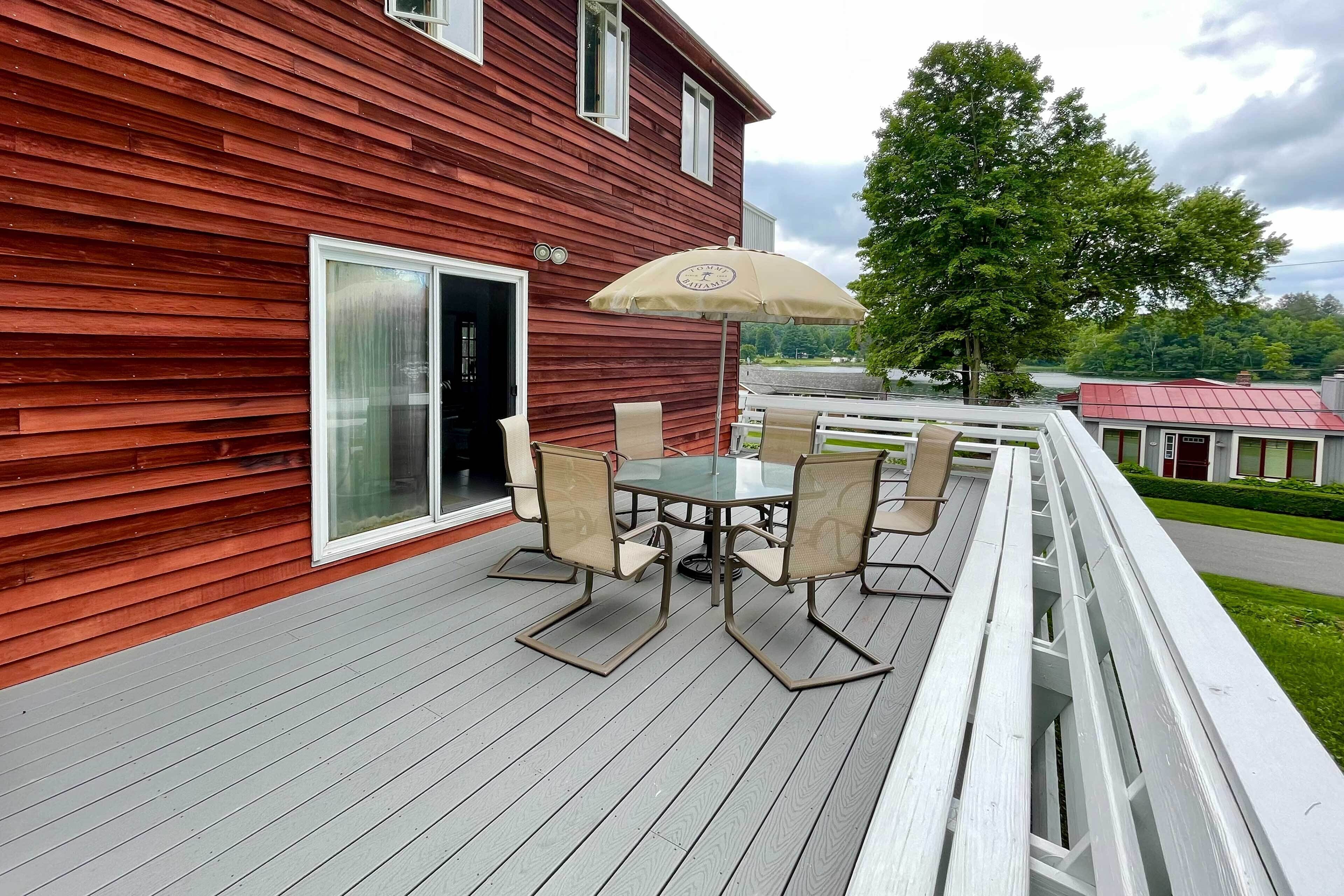 Una terraza roja de madera con puerta de cristal, una mesa con sillas y una sombrilla.