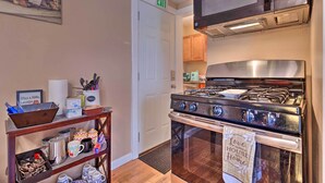 A kitchen with a stove, microwave, and cabinets. There is a shelf with kitchen items and a door with an exit sign.
