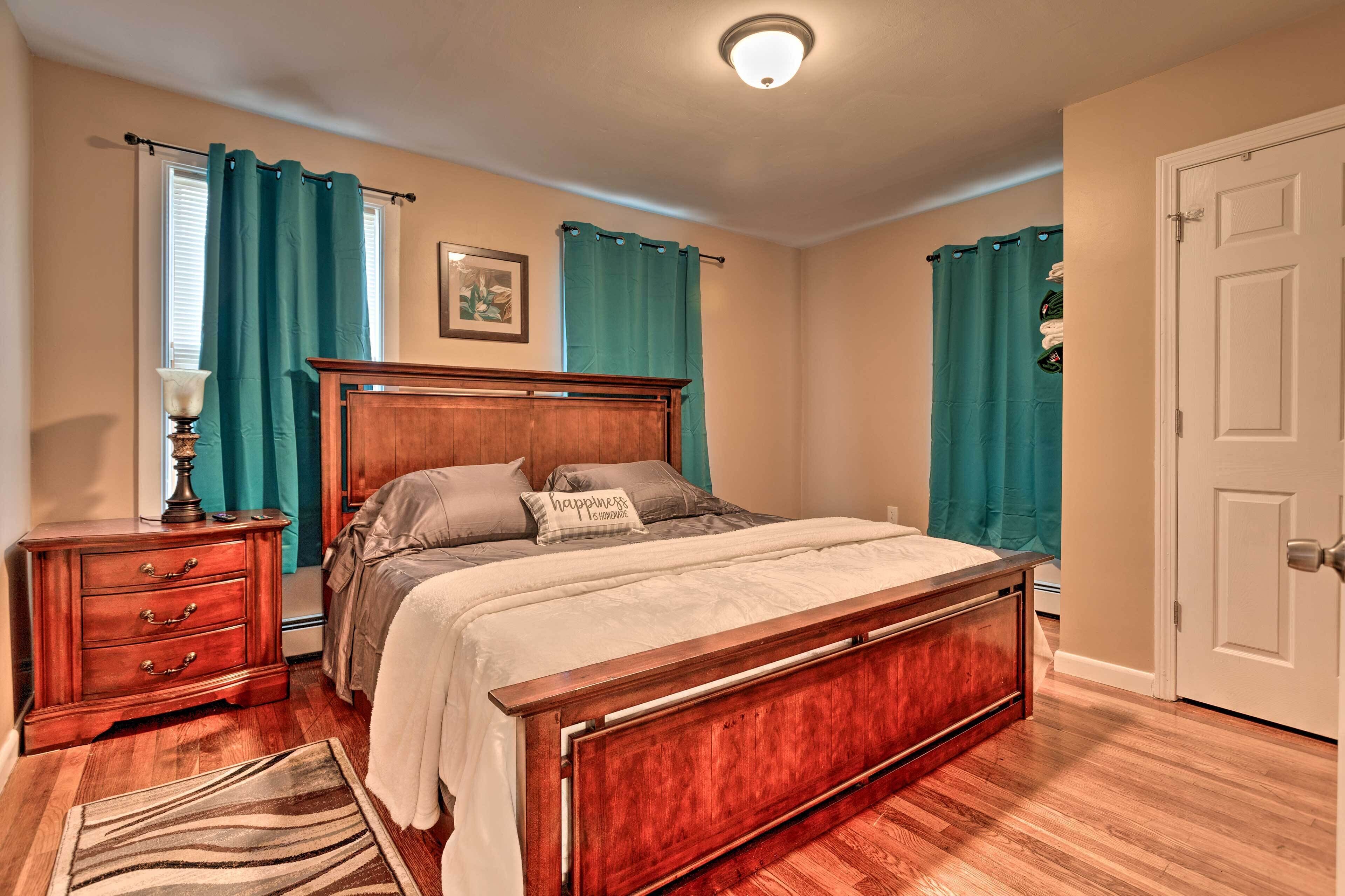 A bedroom with a wooden bed, teal curtains, a nightstand, and a rug.