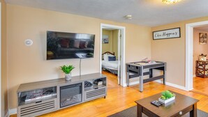 A living room with a flat-screen TV, a wooden coffee table, and a console table with magazines and a plant.