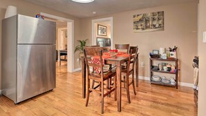 A dining area with a wooden table and chairs, a stainless steel refrigerator, and a wall-mounted shelf with dishes.
