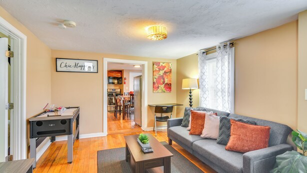 A living room with a sofa, coffee table, and a pool table. There is a kitchen in the background.