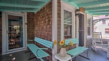 Een veranda met twee turquoise bankjes, een witte tafel met een bloemenvaas, en een bakstenen muur.