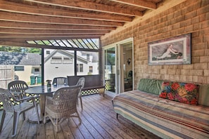 Une terrasse extérieure couverte, avec une table et des chaises en bois, un banc rembourré et un tableau encadré accroché au mur.