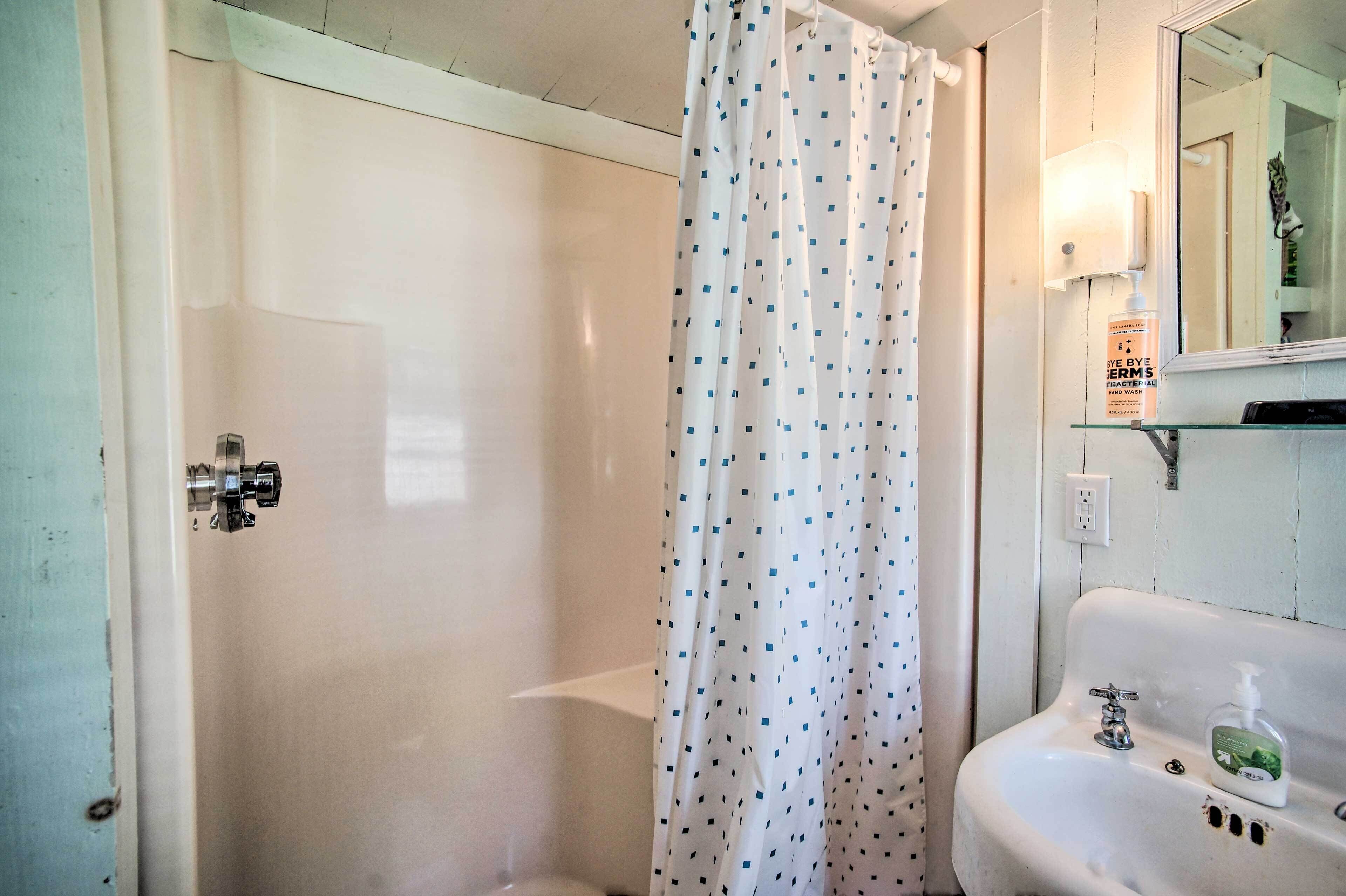 A bathroom with a shower, a sink with a soap dispenser, and a mirror.
