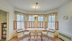 A dining room with a wooden table and chairs, large windows with shutters, a hanging light fixture, and a bookshelf. - Apt on Vineyard Haven Near Nantucket Sound! (Vineyard Haven)