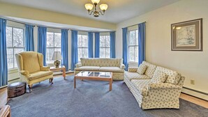 A living room with a sofa, armchair, and coffee table, large windows with blue curtains, and a chandelier. - Apt on Vineyard Haven Near Nantucket Sound! (Vineyard Haven)