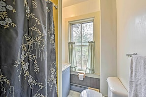 Ein Badezimmer mit Fenster, Toilette und einer Duschvorhang mit floralem Muster.