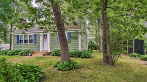 A green house with a front porch, surrounded by trees and shrubs.