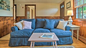 A blue sofa with a small table in front, a lamp on a side table, and a window with blinds.