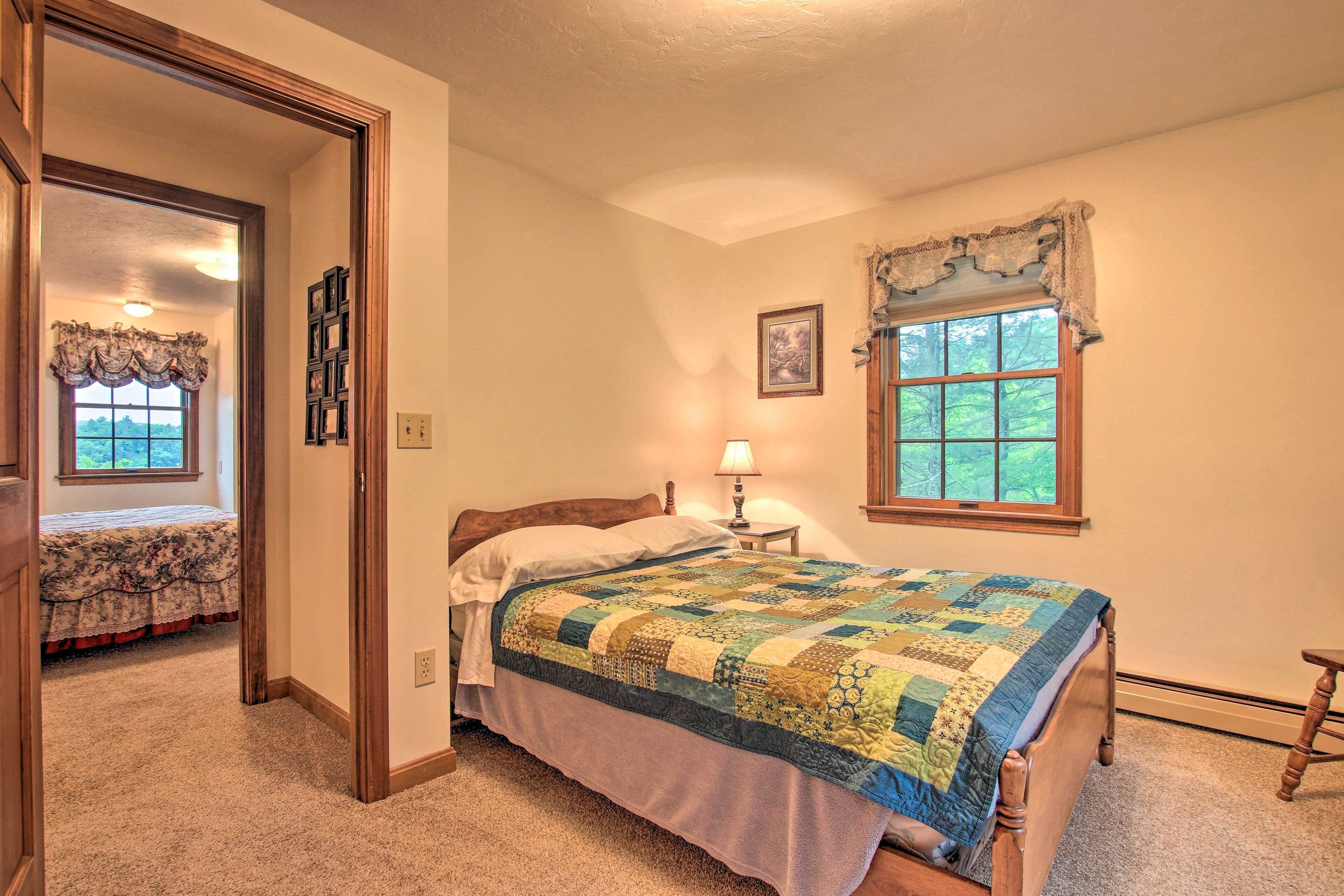 A bedroom with a large bed, a window with a valance, a bedside lamp, and a door leading to another room.
