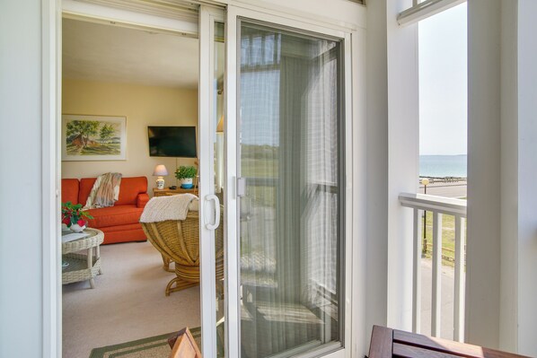 A balcony with a view of the ocean, a wicker chair, a sofa, and a small table with a lamp.