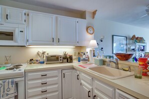 A kitchen with white cabinets, a microwave, a toaster, a sink, and various kitchen items on the counter.