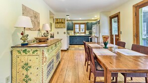 Une cuisine avec des meubles de rangement en bois, une table à manger avec des chaises et un îlot central décoratif agrémenté d’une lampe.