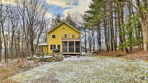 Une cabane jaune avec un porche vitré, entourée d’arbres et recouverte de neige.