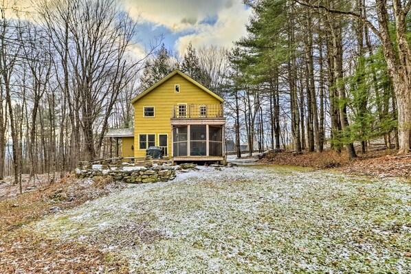 A yellow cabin with a glass front porch, surrounded by trees and a snowy ground.