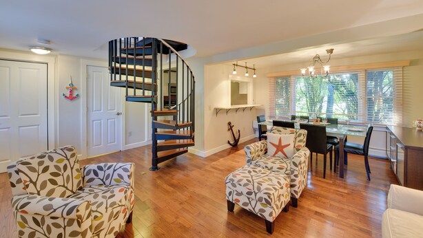 A spacious living area with a wooden floor, a spiral staircase, and a dining area with a glass table and chairs. - Shop, Dine, Explore Commercial St! Coastal Retreat (Provincetown)