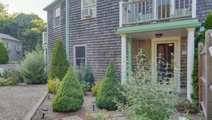 A two-story house with a front porch, a gravel driveway, and various shrubs and plants. - Shop, Dine, Explore Commercial St! Coastal Retreat (Provincetown)
