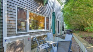 A patio area with a table and chairs, a covered grill, and an air conditioning unit. - Shop, Dine, Explore Commercial St! Coastal Retreat (Provincetown)