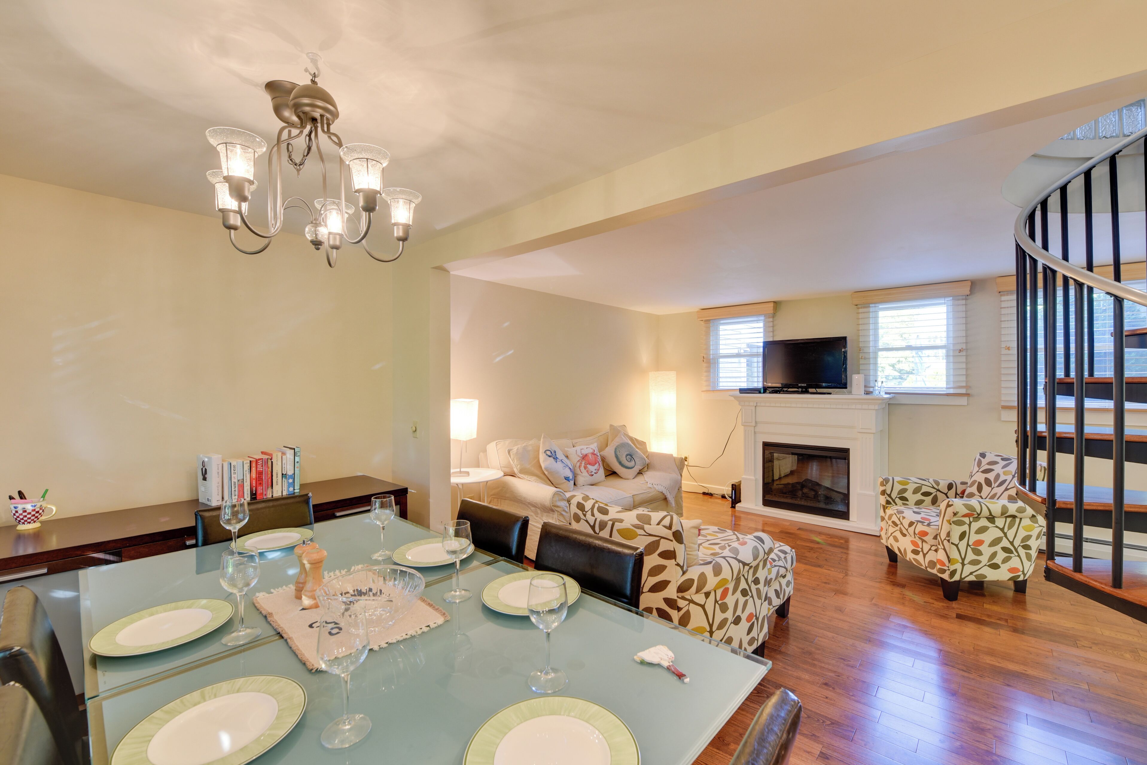 A dining area with a table set for four, a fireplace, a sofa, and a staircase.