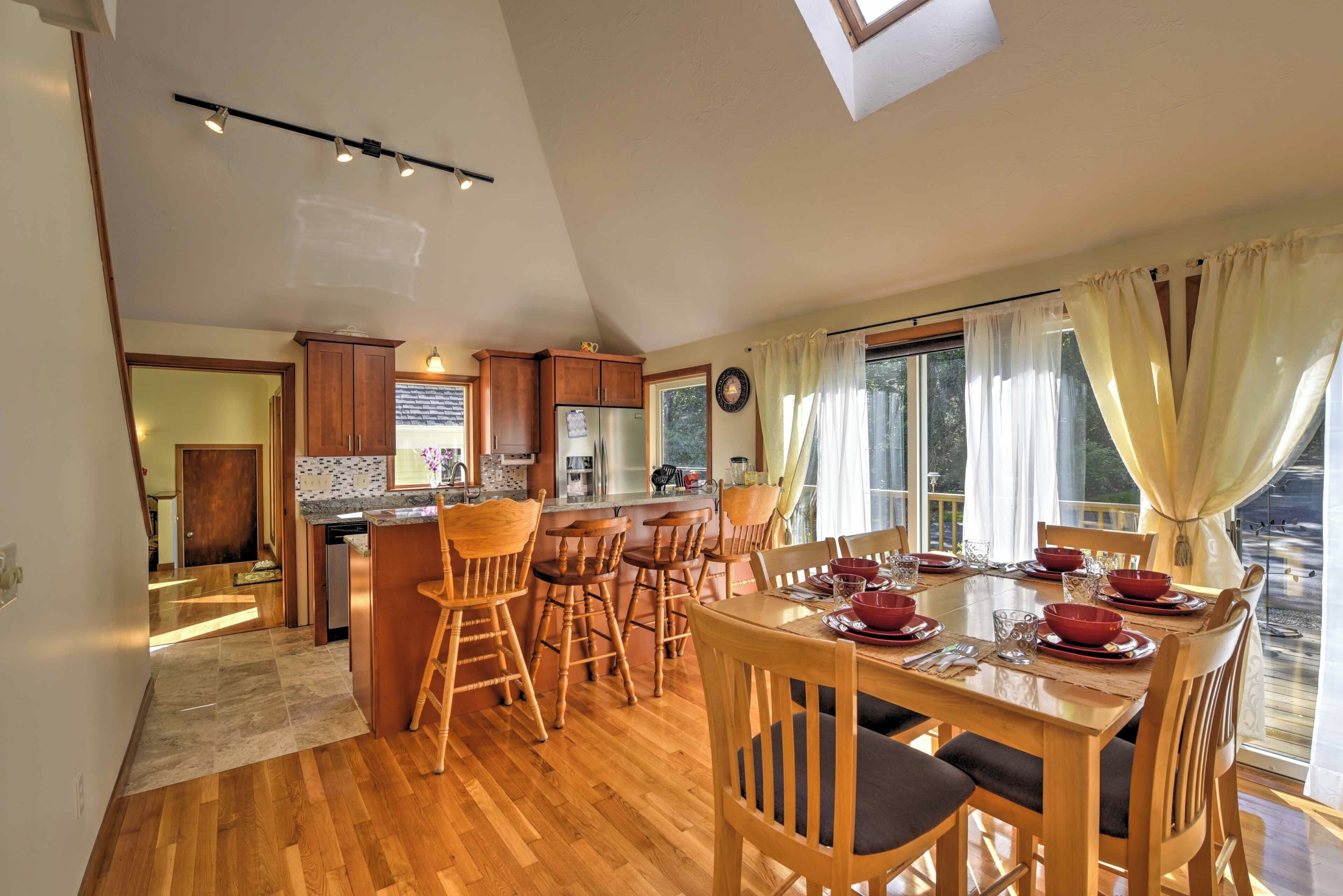 A spacious kitchen with wooden cabinets, a dining area with a large table set for six, and a view of the outdoors through large windows.
