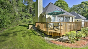 A house with a wooden deck, a covered patio, and a large window overlooking a garden.