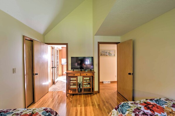 A room with wooden flooring, a television on a wooden stand, and a bed with a floral bedspread. - Families Welcome! East Falmouth Home 4 Mi to Beach (East Falmouth)