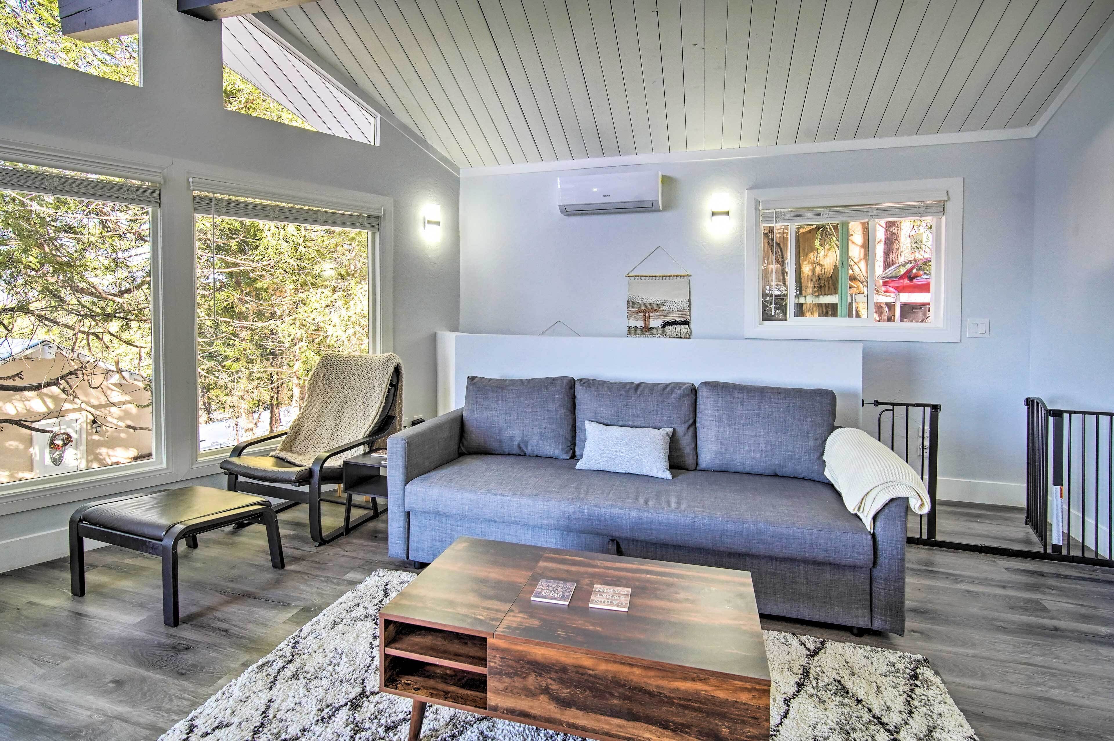 A living room with a grey sofa, a wooden coffee table, and a large window.