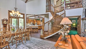 A spacious living area with a dining table, chairs, a sofa, a staircase, and a kitchen in the background. - Ornate Lake Arrowhead Home With Deck (Lake Arrowhead)