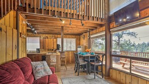 Ein Interieur einer Holzhütte mit einem roten Sofa, einer Holzbalkendecke, einem Essbereich und großen Fenstern mit Blick auf eine Terrasse.