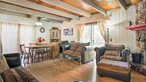 A cozy living room with wooden floors, a dining area with a wooden table and chairs, and a fireplace with a stone wall.
