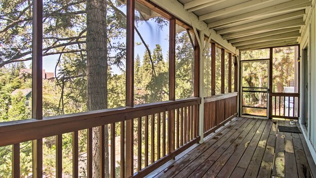 A covered wooden deck with large windows overlooking a forested area.