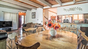 A spacious living room with a wooden dining table, comfortable seating, a flat-screen TV, and a kitchen in the background.