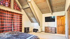 A bedroom with a bed, a wooden ceiling, a fireplace, a television, and a door.