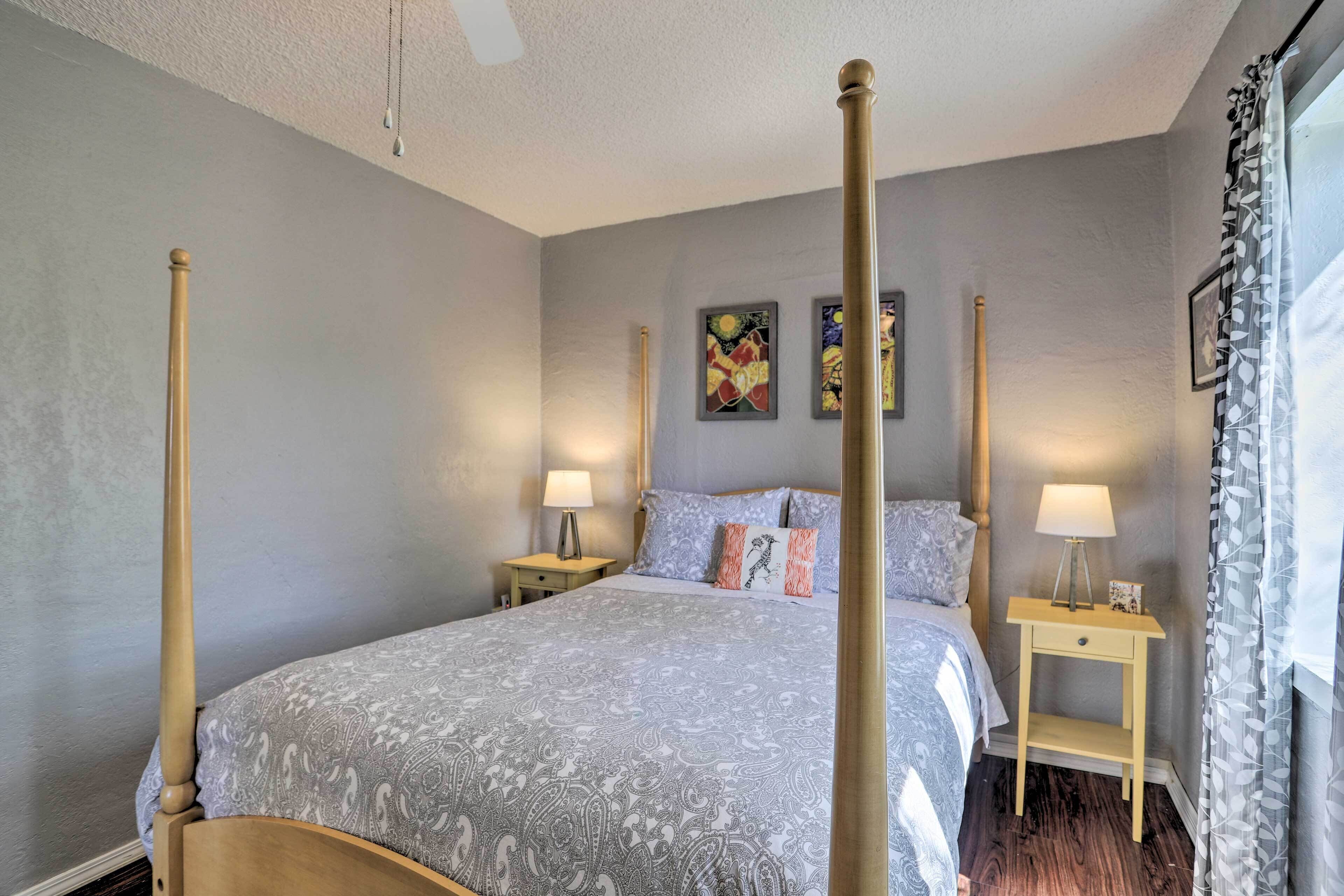 A four-poster bed with a patterned bedspread, two bedside tables with lamps, and artwork on the wall.