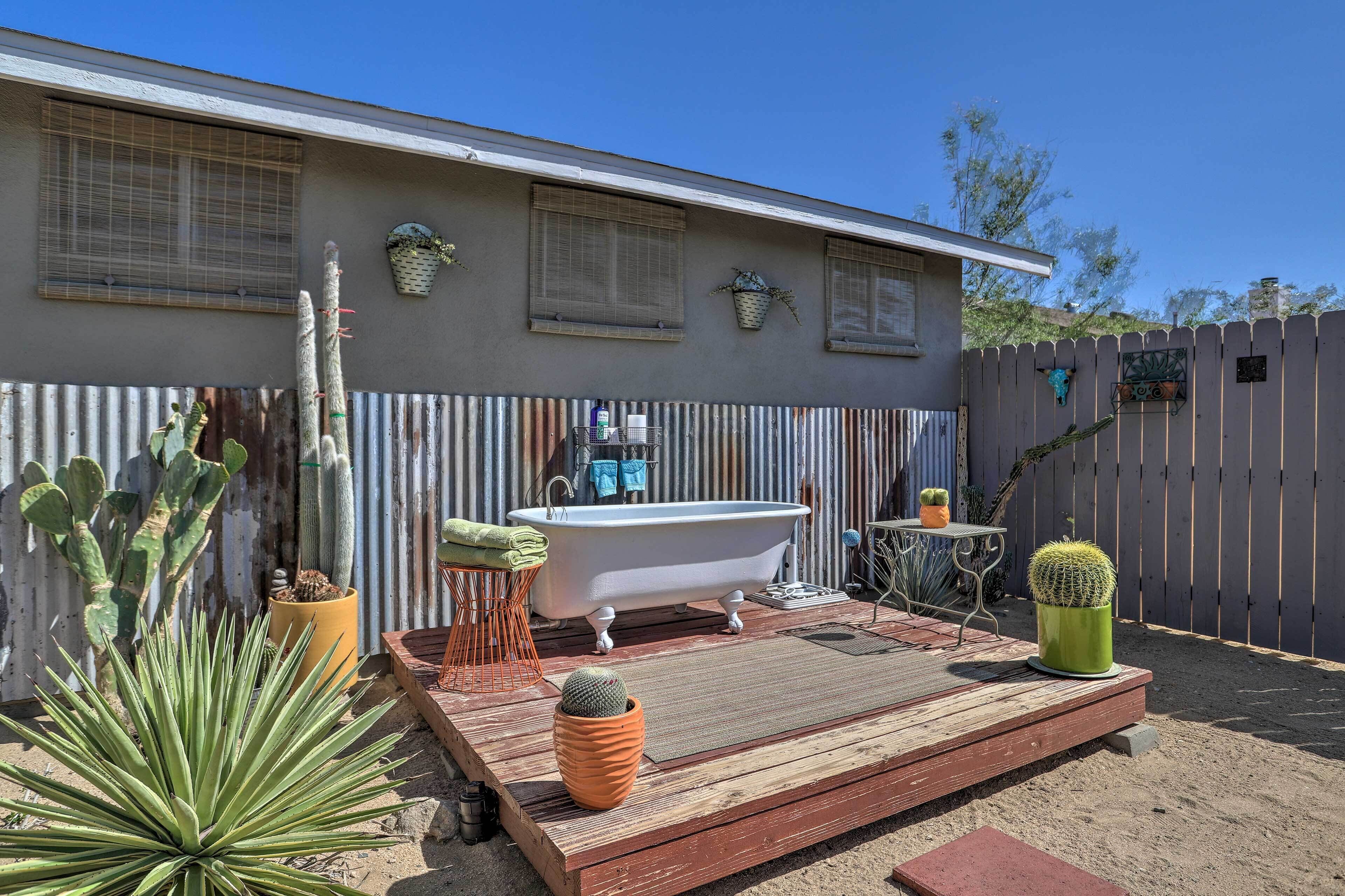 Een terras met een vintage badkuip, potten met cactussen en een houten terras.