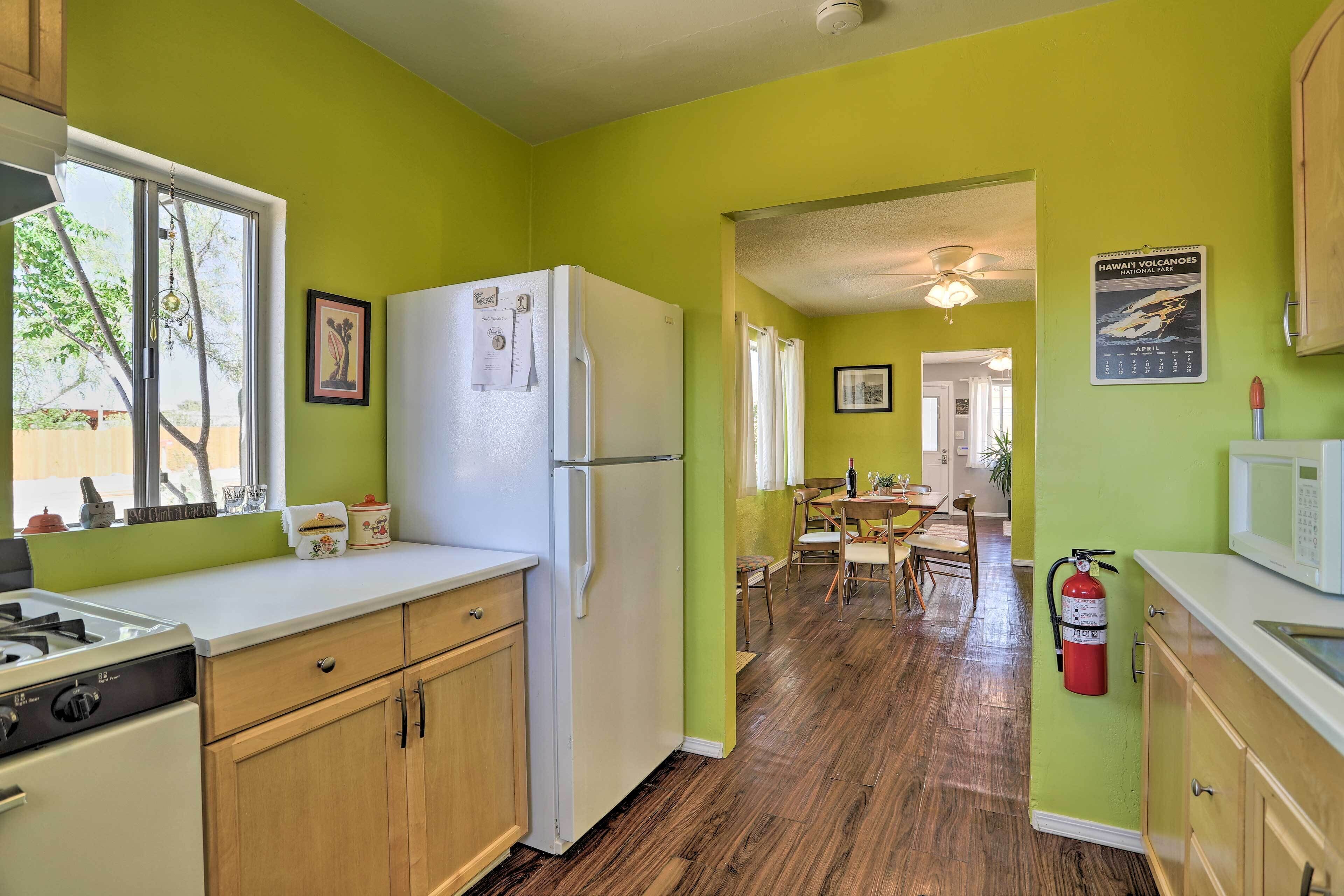 Una cocina con refrigerador, estufa y armarios de madera. Hay una zona de comedor con mesa y sillas, y un pasillo que conduce a otra habitación.