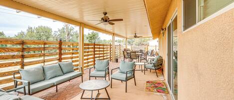 An outdoor patio with a wooden ceiling, ceiling fans, a sofa, chairs, a table, and a view of the surrounding landscape.