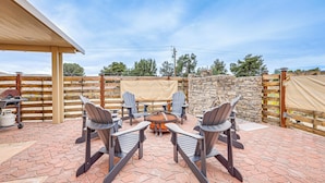 Eine Terrasse im Freien mit Steinboden, einer runden Feuerstelle und vier Adirondack-Stühlen.
