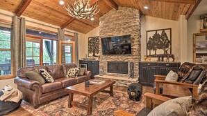 A cozy living room with a stone fireplace, leather furniture, and a large TV. - Near Bear Mountain & Big Bear Lake: Gem w/ Hot Tub (Big Bear City)