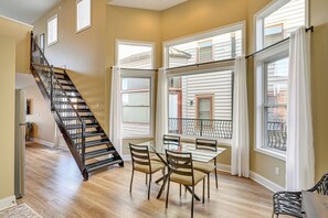 Un comedor con mesa y sillas, una escalera y ventanas amplias con cortinas.