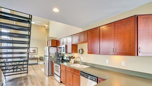A modern kitchen with wooden cabinets, stainless steel appliances, and a black metal staircase.