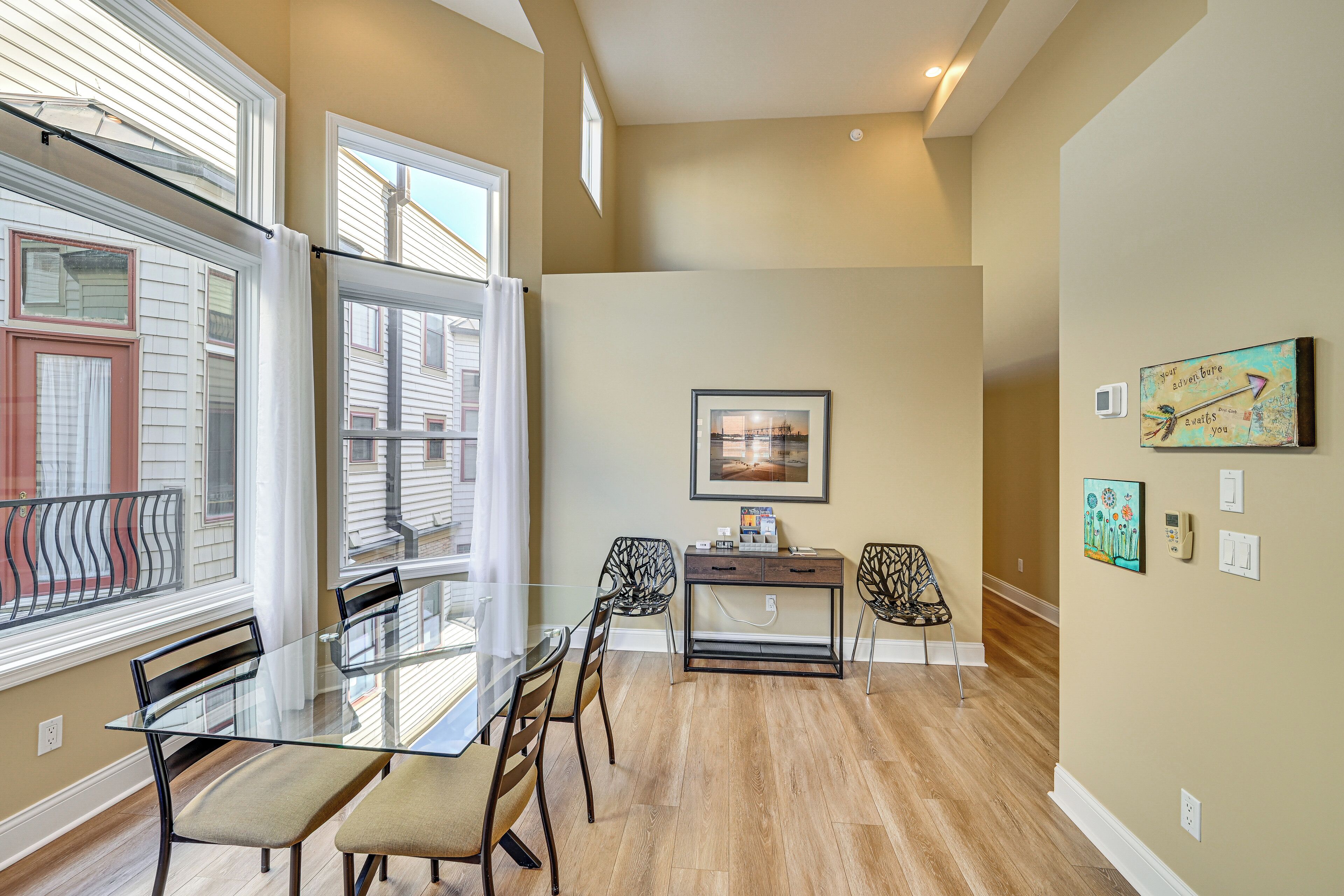 A dining area with a glass table and chairs, a small side table, and a wall-mounted artwork.