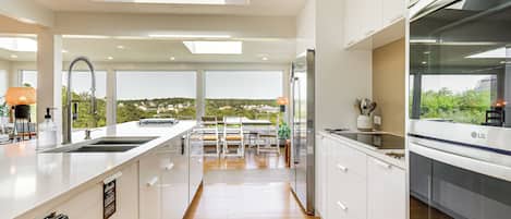 Une cuisine moderne avec des meubles blancs, un grand îlot central et une vue sur l’extérieur.