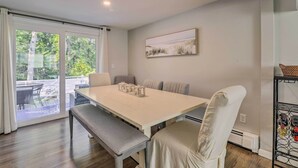 Uma área de refeições com uma mesa, cadeiras e um banco. Há uma porta de vidro que dá para uma área externa com mesa e cadeiras. Um quadro está pendurado na parede acima da mesa.