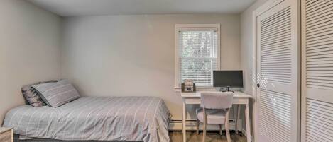 A bedroom with a bed, a desk, a chair, and a window.